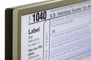 IRS Form 1040 displayed on an LCD computer screen using very shallow depth of field (DOF). Focus is on "Form 10". First Name field is being filled out (1st 2 letters typed).