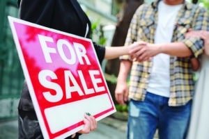 Real estate agent holding for sale sign and shaking hand of customer